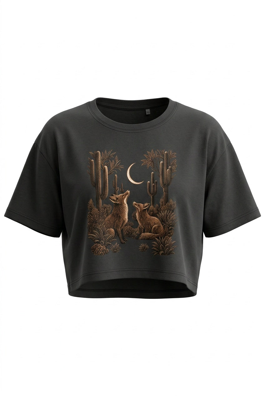 A dark charcoal gray cropped t-shirt featuring a detailed graphic print of desert cacti, coyotes, and a crescent moon in earthy brown and tan tones, displayed against a solid white background.