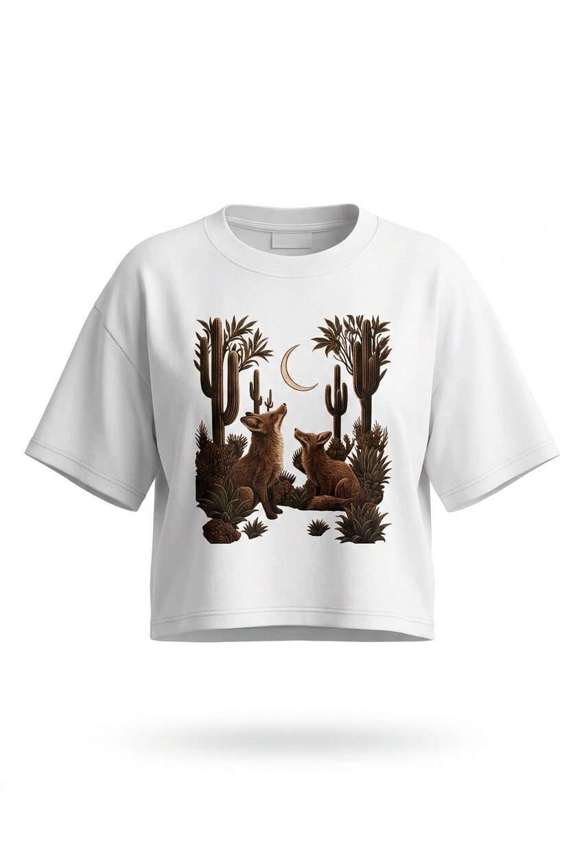 A white short-sleeve crop top t-shirt featuring a graphic print of two brown foxes sitting among cacti under a crescent moon.
