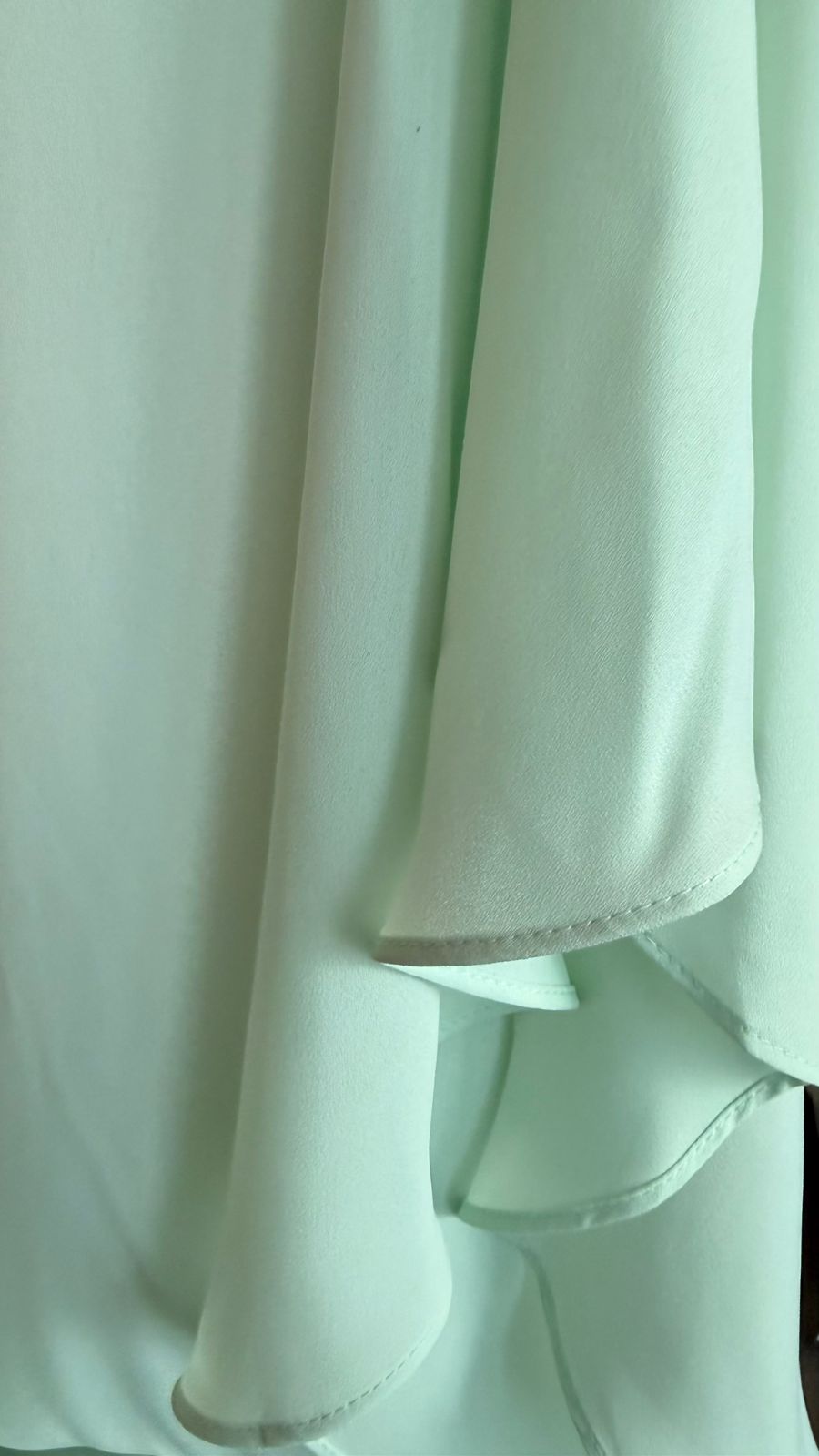 A close-up of a light mint green fabric garment, showing the soft texture and draped folds of the material.