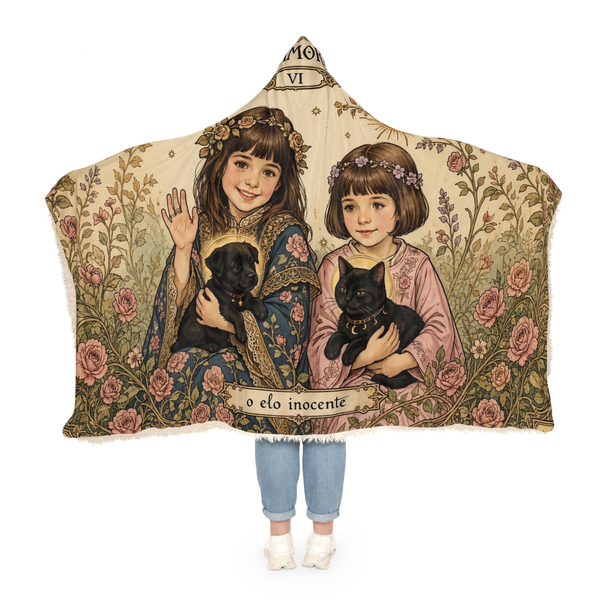 A hooded throw blanket featuring a vintage-style illustration of two girls holding black cats, with floral borders and the text 'o elo inocente' across the bottom. The blanket is shown on a white background with a child's legs and feet visible underneath.