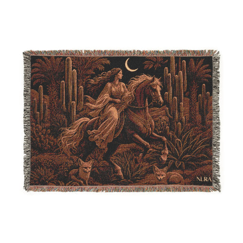 A woven tapestry throw blanket featuring a desert night scene with a woman riding a horse, cacti, desert plants, and a crescent moon, finished with fringe on the edges.