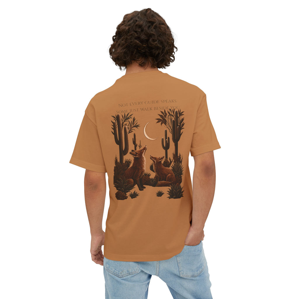 A man viewed from behind wearing a rust-orange t-shirt with a detailed desert graphic of coyotes, cacti, and a crescent moon on the back, paired with light blue jeans against a plain white background.