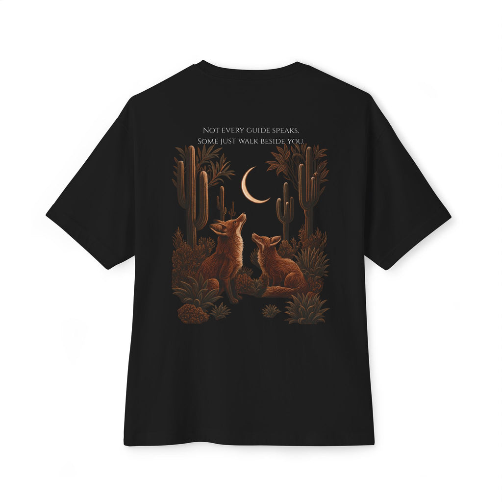 A black short-sleeve t-shirt shown flat against a white background, featuring a detailed graphic print on the back with two brown foxes under a crescent moon in a desert landscape with cacti, and the text 'NOT EVERY GUIDE SPEAKS. SOME JUST WALK BESIDE YOU.