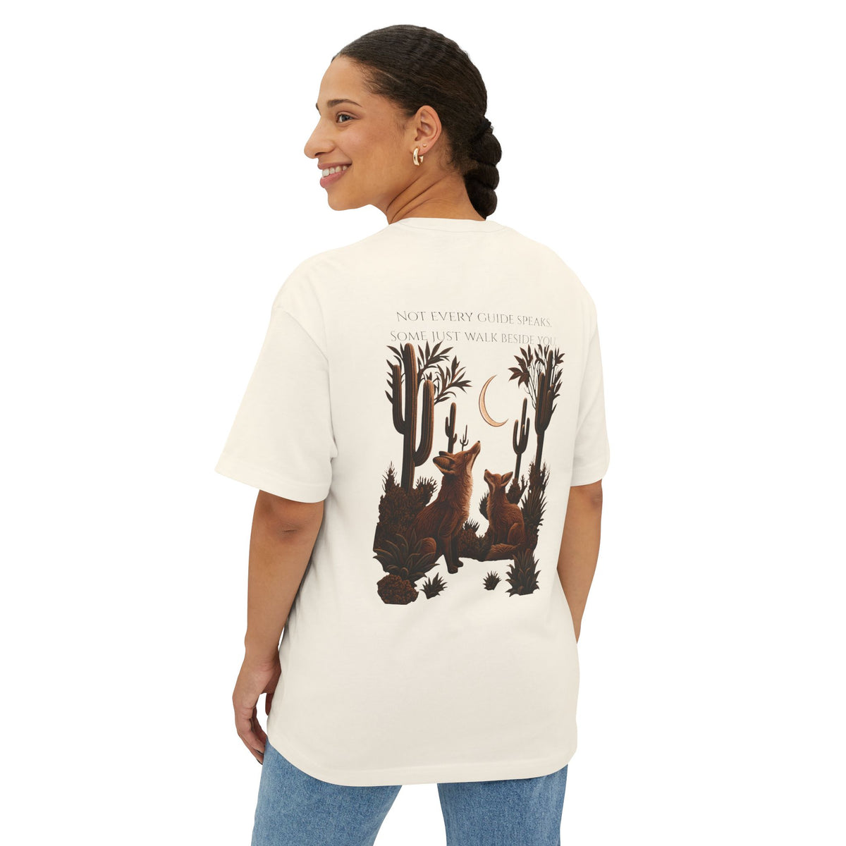 A woman shown from the back wearing an off-white graphic t-shirt with a desert scene print featuring two foxes, cacti, and a crescent moon, paired with blue jeans against a plain white background.